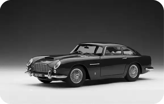 Black-and-white studio photograph of an Aston Martin DB5 against a dark backdrop