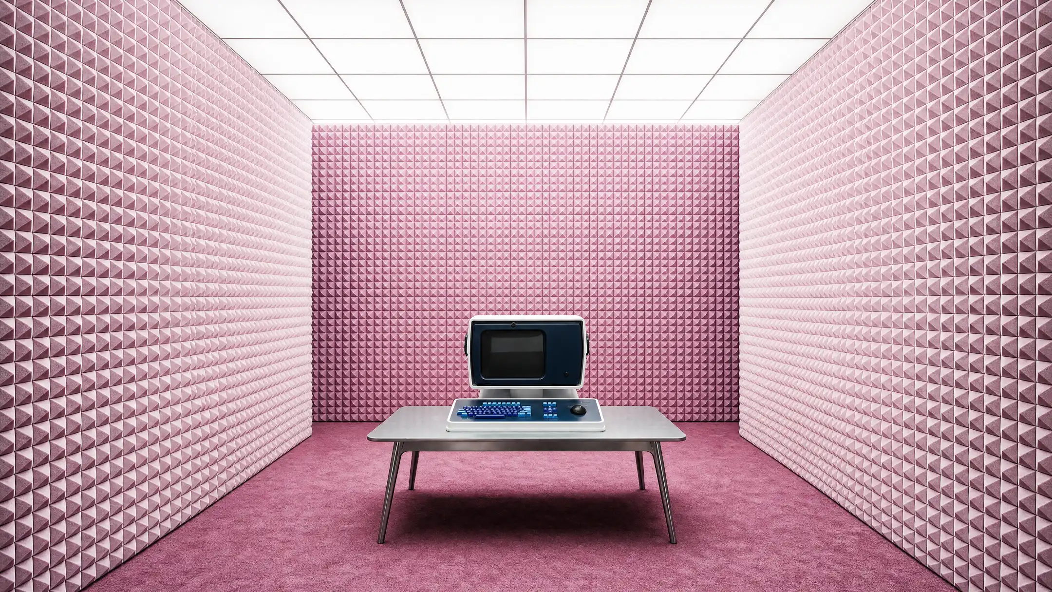 A small pink room lined with acoustic foam, with a retro computer terminal on a steel table under a glowing ceiling